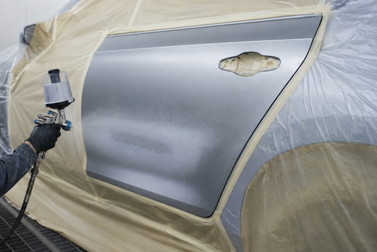 Photo depicts an individual using a spray gun to blend a vehicle panel.